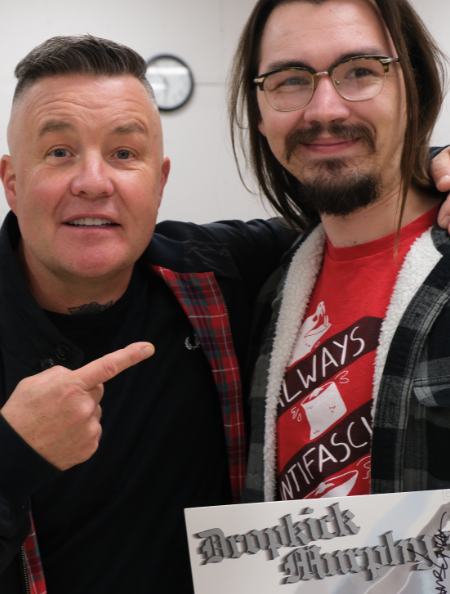 Two men, Ken Casey of the band Dropkick Murphys and Dalton Erickson, standing together. Casey is pointing at Erickson, and Erickson is holding signed copy of Dropkick Murphys' first album. 