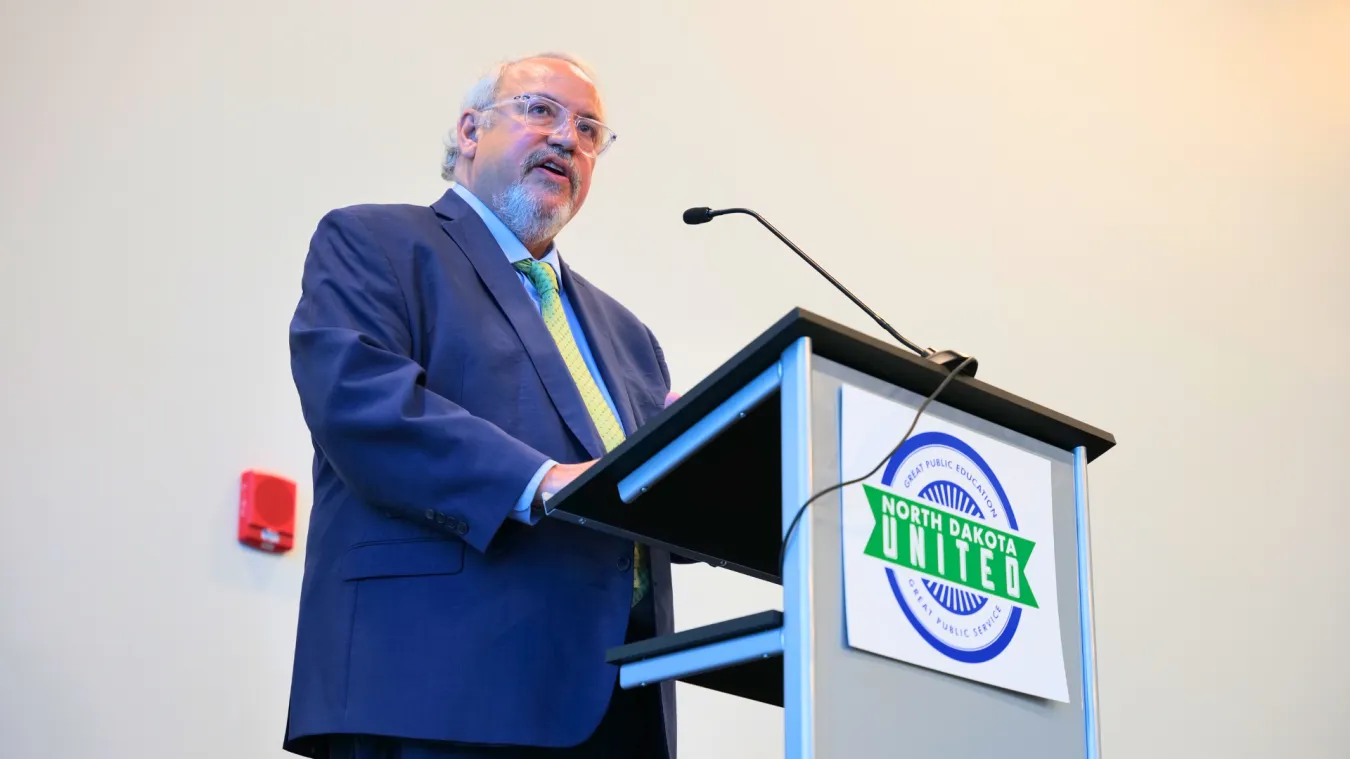 man in blue suit giving speech at a podium