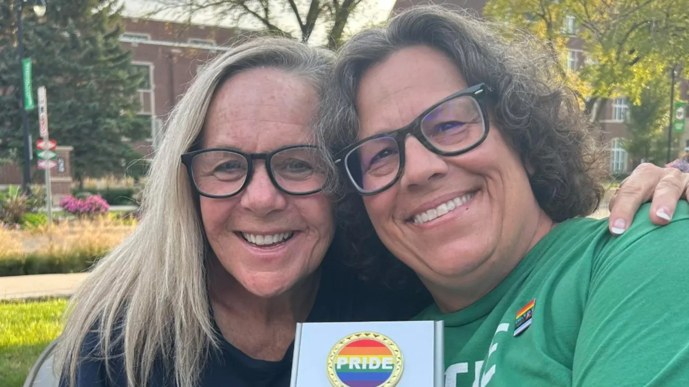 Two women outside on a college campus, holding a plaque that reads "Pride."