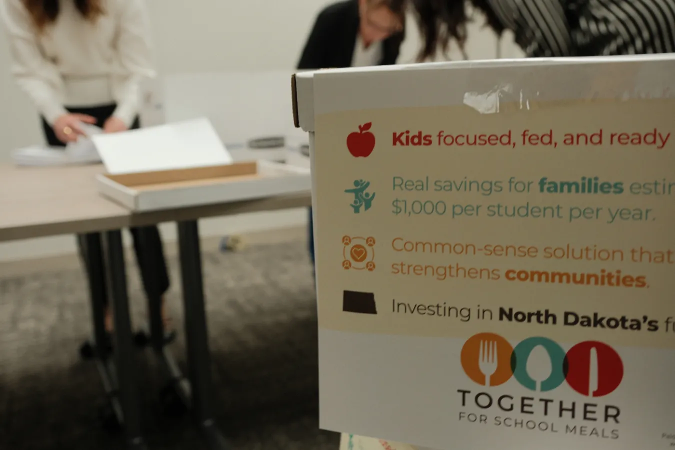 A box labeled with campaign messaging sits in the foreground as Secretary of State staff sort petition sheets in the background.