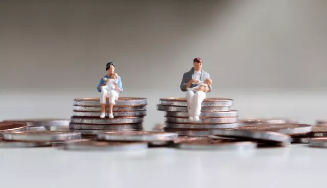 Small doll parents holding babies sits on top of stacks of coins.