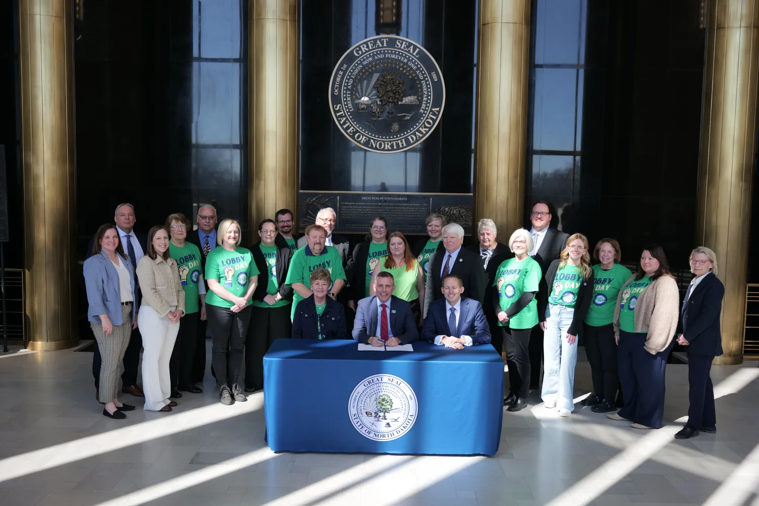 group of people standing around nd gov. while he signs a bill