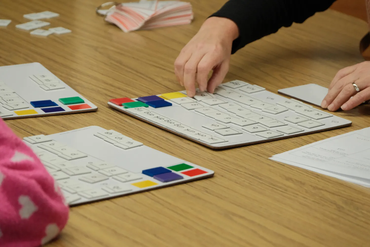 Close-up of a teacher’s hands arranging letter tiles on a tabletop as part of a phonics or literacy activity.