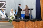 high school student wearing cap and gown getting their diploma