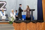 high school student wearing cap and gown getting their diploma