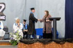 high school student wearing cap and gown getting their diploma