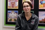 Classroom scene with Laine Hernandez, Spanish teacher, sitting in front of wall of photos.