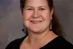 headshot of woman with black top and hair pulled back