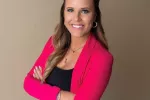 woman wearing blazer with her arms crossed smiling