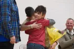 Woman hugging elementary school student holding flowers