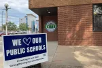 Exterior of office building, with North Dakota United logo on brick wall, and "We Love Our Public Schools" sign in foreground.