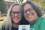 Two women outside on a college campus, holding a plaque that reads "Pride."