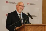 North Dakota United President Nick Archuleta stands at a podium with microphones in front of a North Dakota Department of Public Instruction backdrop.