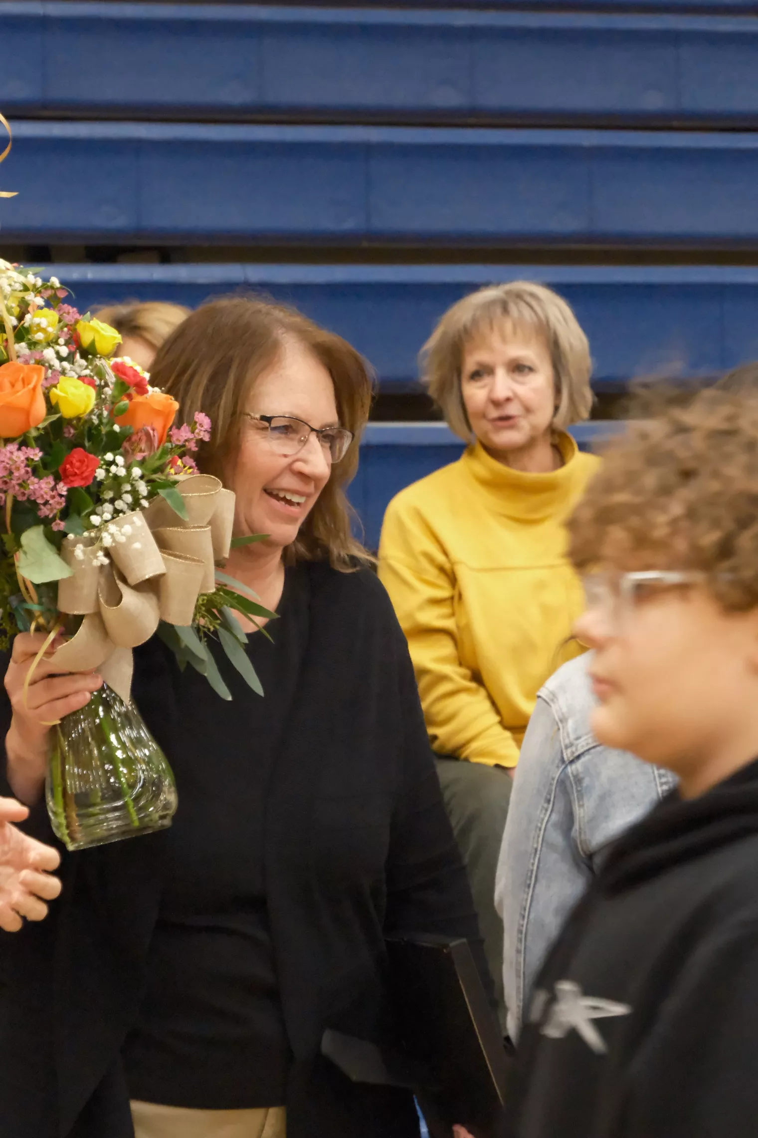Brenda Muller holding a vase of flowers given to her with award at ceremony held in Hillsboro gymnasium.
