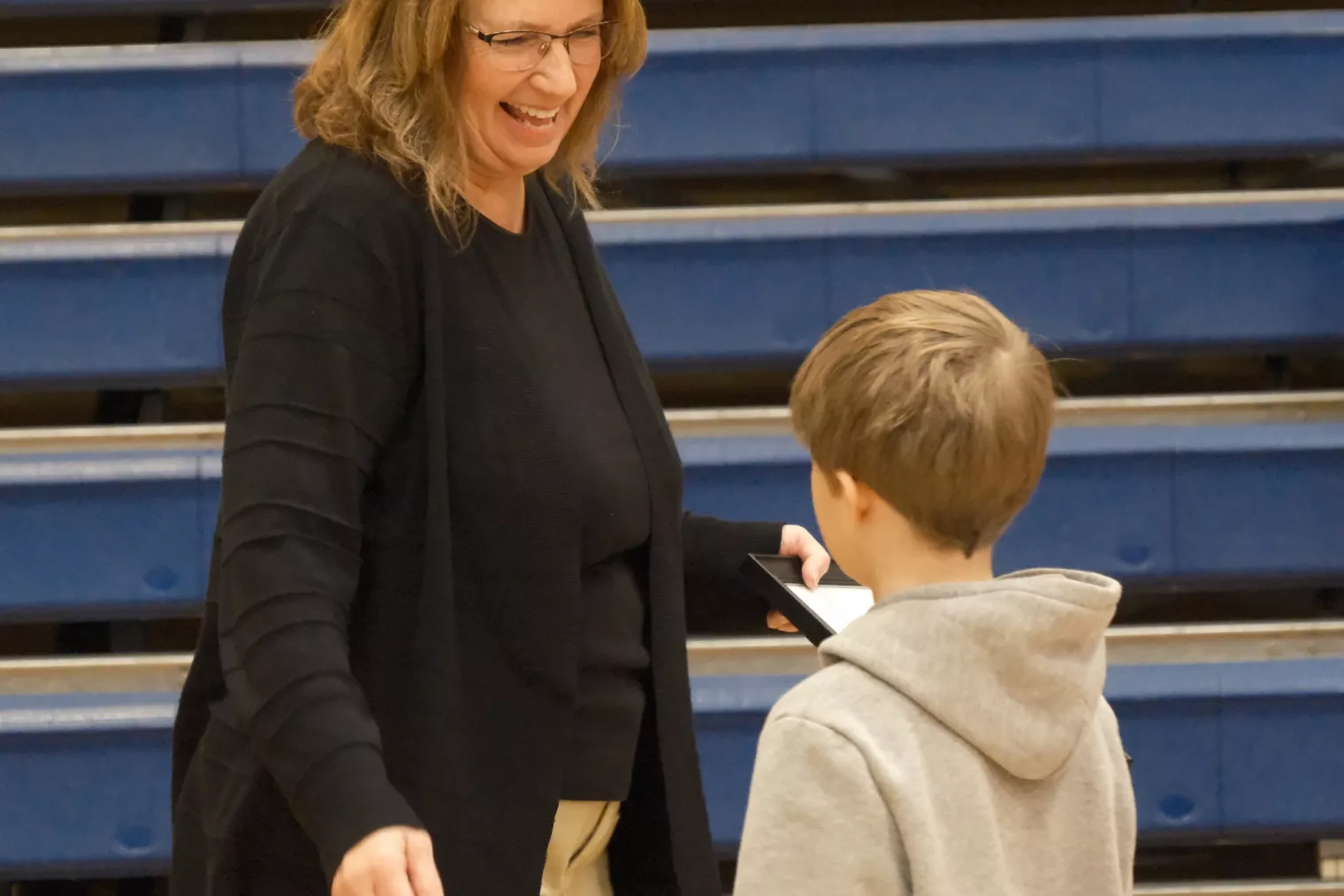 ESP of the Year finalist Brenda Muller smiles down at student who is congratulating her at award ceremony in gymnasium.