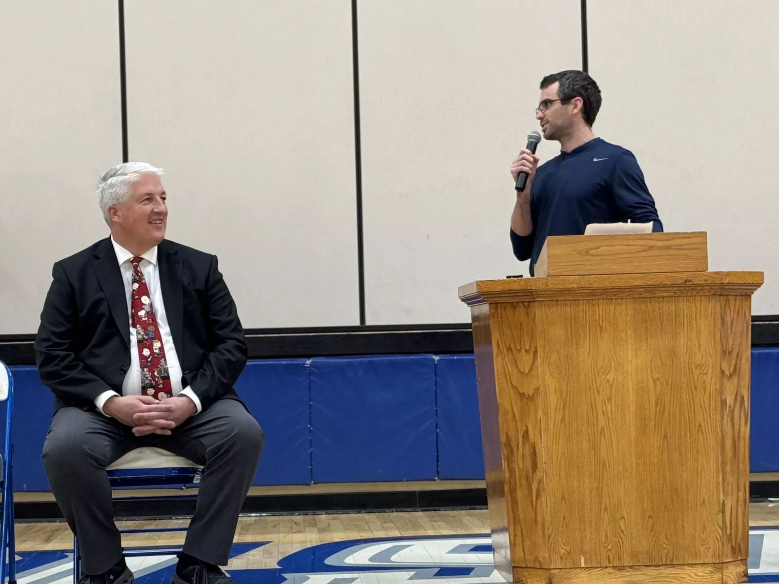 Elementary principal speaks at podium in Hillsboro school gymnasium for event celebrating ESP of the Year finalist, which superintendent looks on.