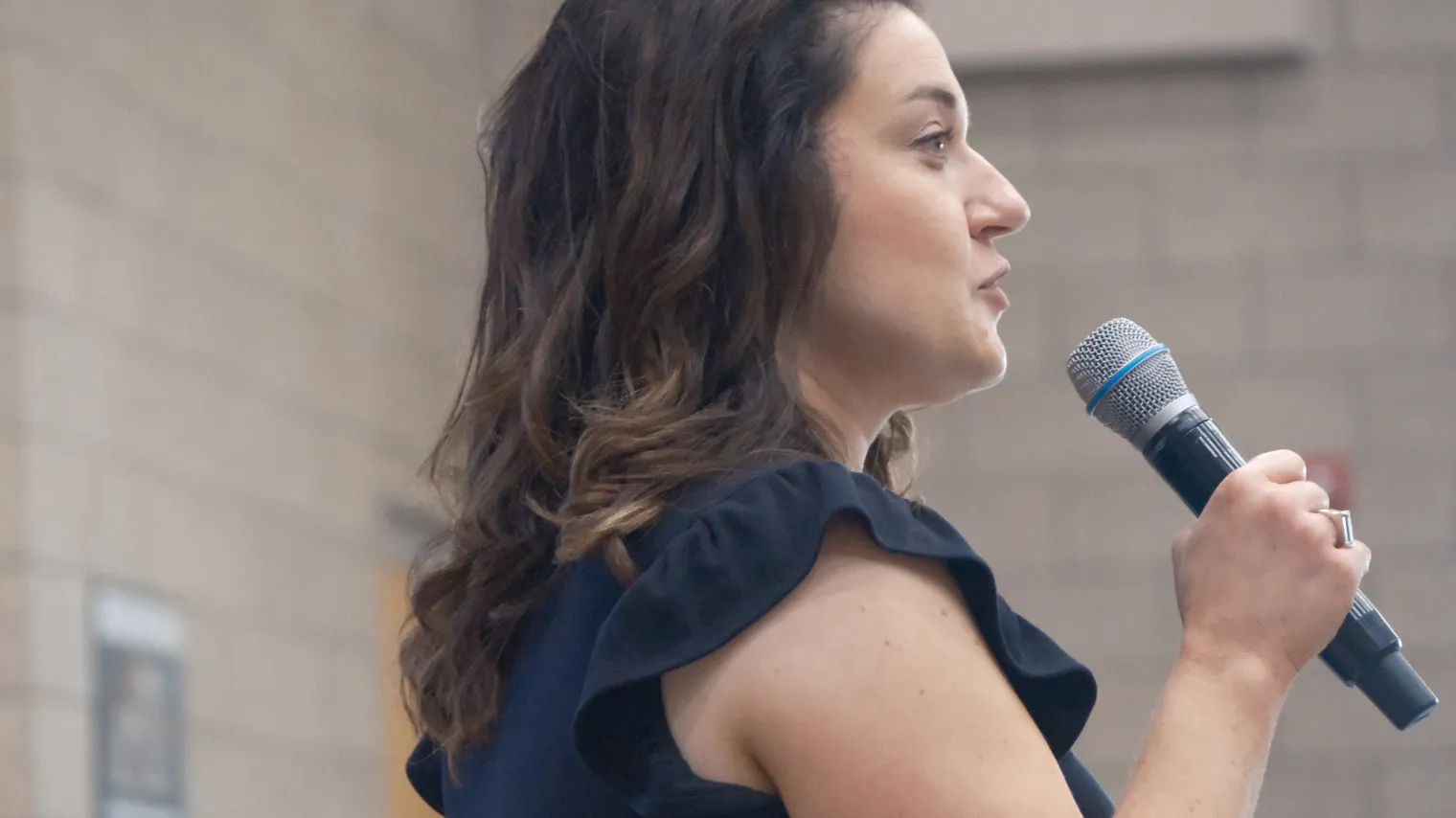 Woman with microphone speaking in school gymnasium.
