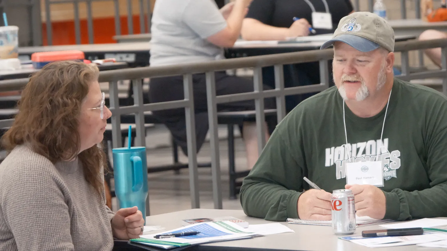 Man and woman having conversation at table in school cafeteria.