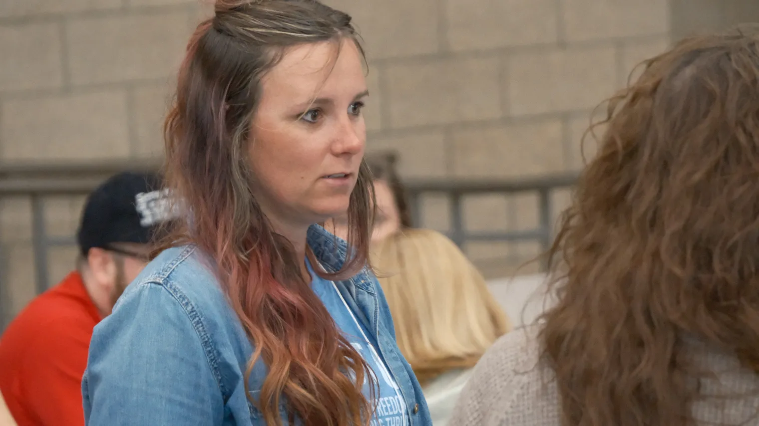 Young woman standing in a group, discussing with others, inside school cafeteria setting.