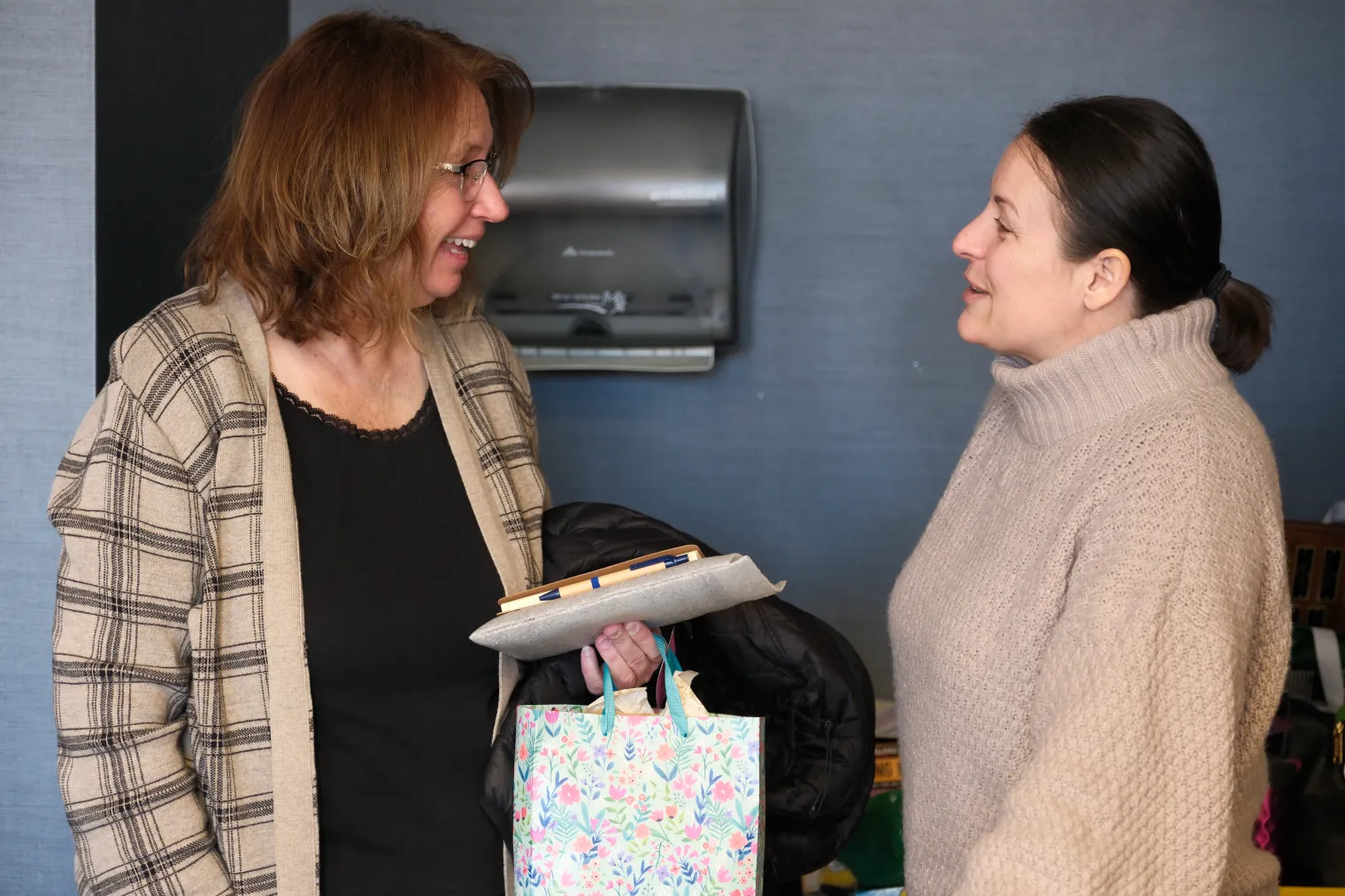 Two women, one holding gift bag and award plaque, having a friendly conversation.