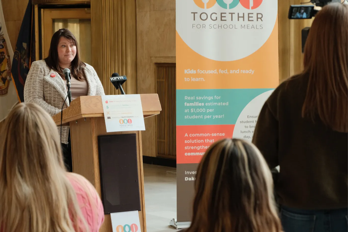 A speaker presents in front of a campaign banner as attendees listen.