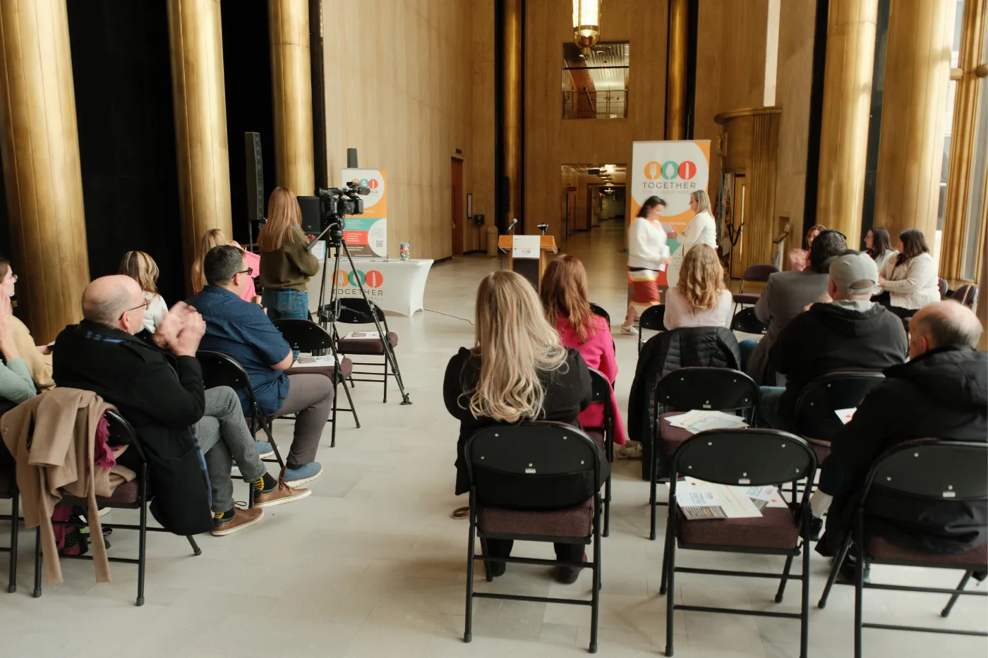 Wide view of the press conference shows attendees, media equipment and speakers in the Capitol.