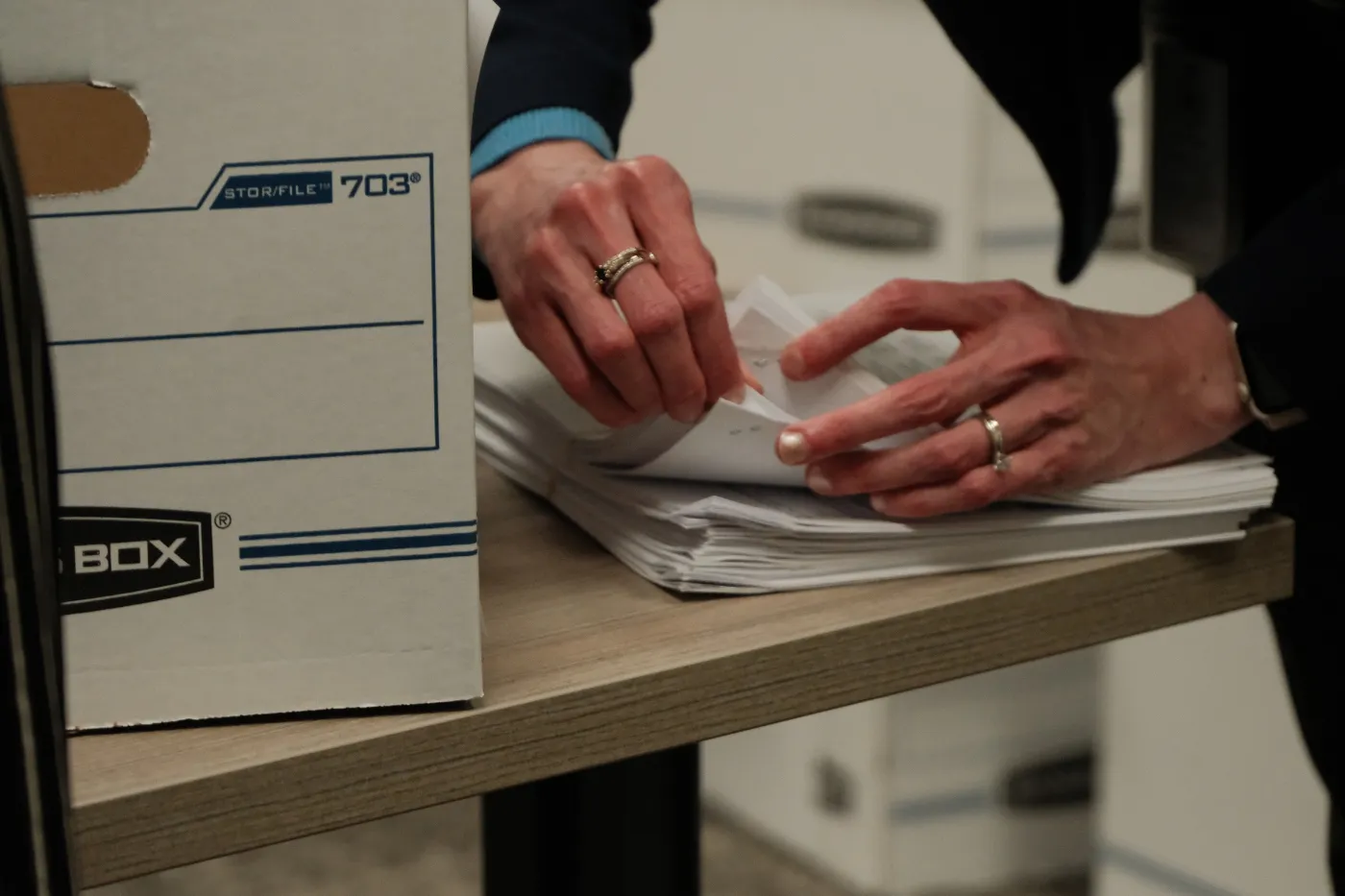 Hands sort and stack petition sheets beside a storage box during signature processing.