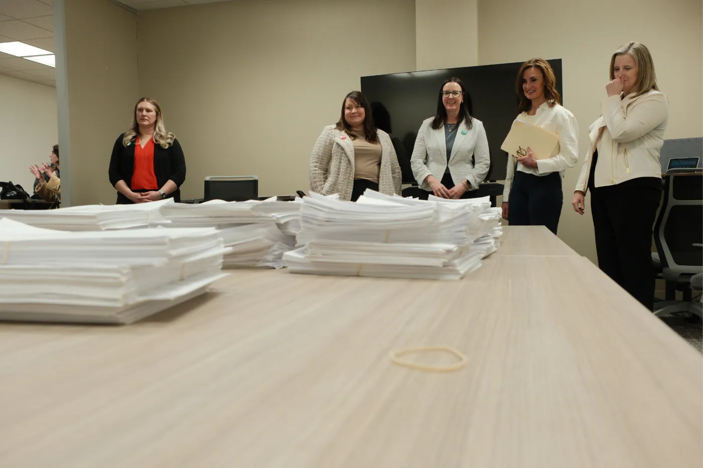 Large stacks of petition signatures sit on a table as coalition members stand nearby reviewing the materials.