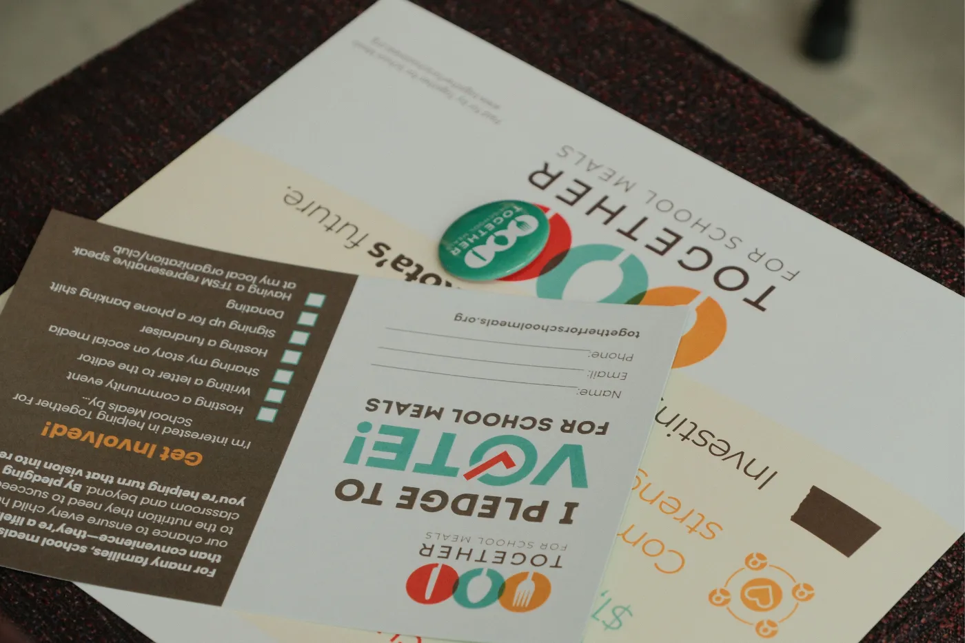 “Together for School Meals” flyers and a campaign button displayed on a table.