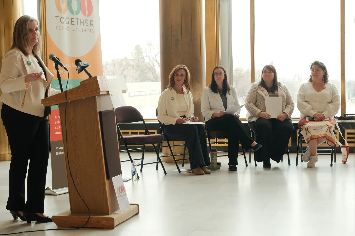 A speaker presents at a podium while panelists sit nearby during the Capitol press event.