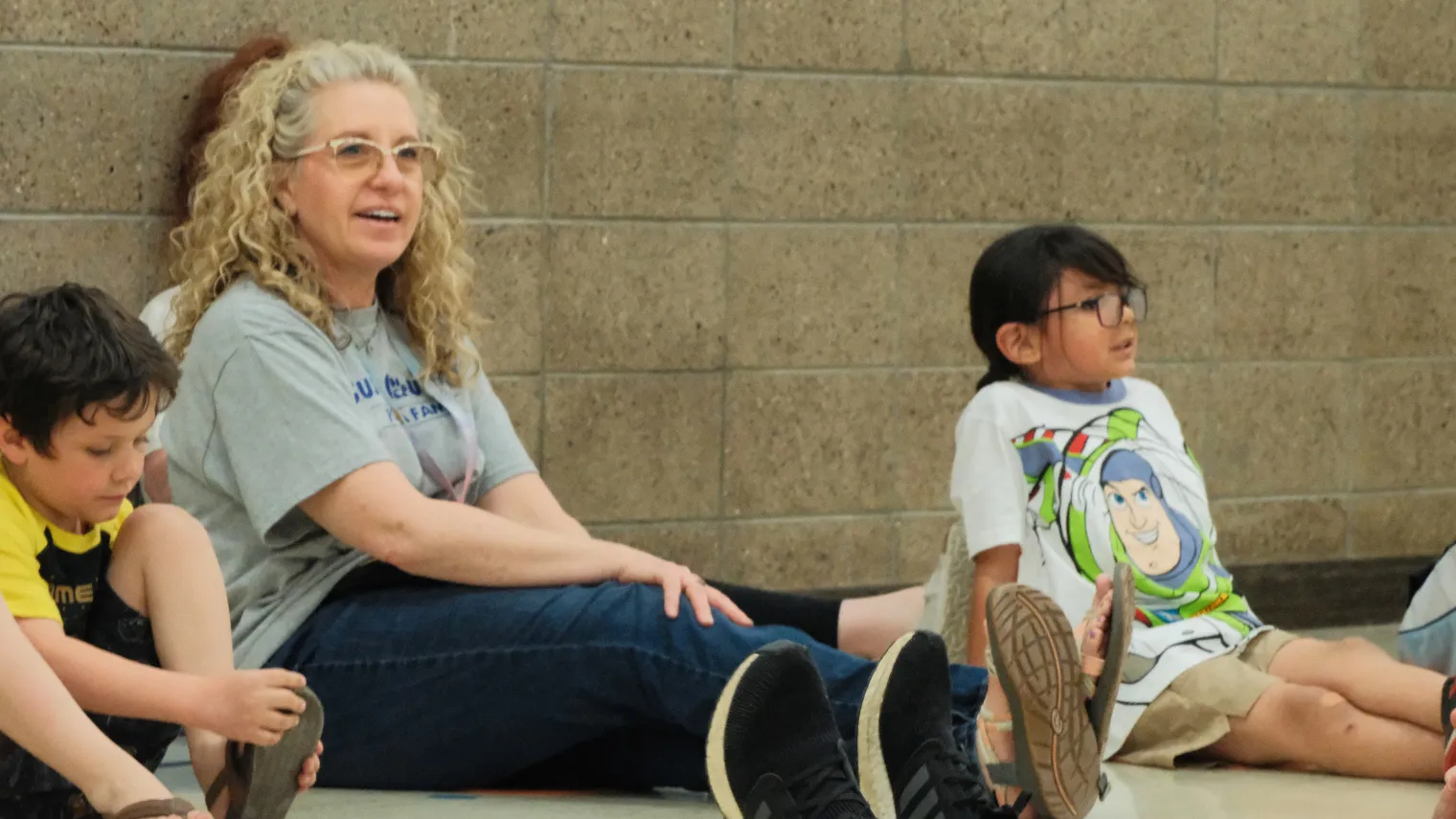 2027 North Dakota United Education Support Professional of the Year Dawn Ressler sits on a school gym floor with elementary students during a physical therapy activity, smiling as they participate together.