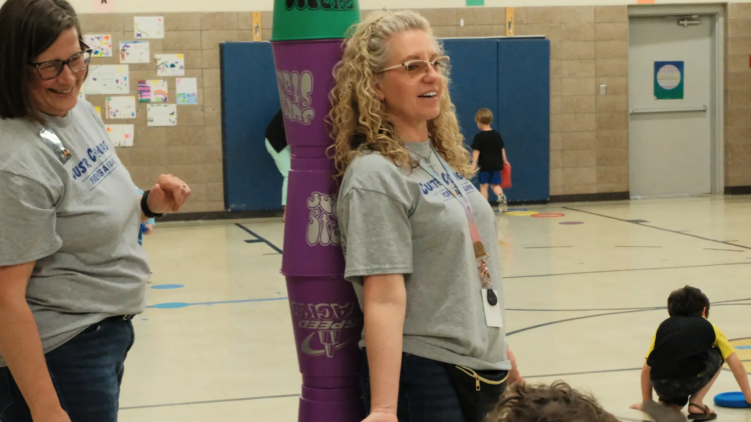 Dawn Ressler smiles while watching students participate in a physical therapy activity in a school gymnasium.