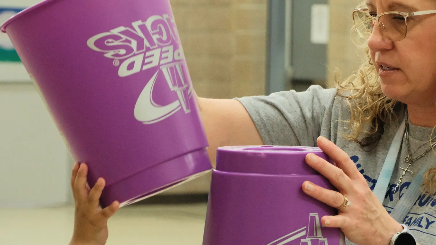Dawn Ressler helps a student stack large plastic buckets during a hands-on activity that builds coordination and motor skills.