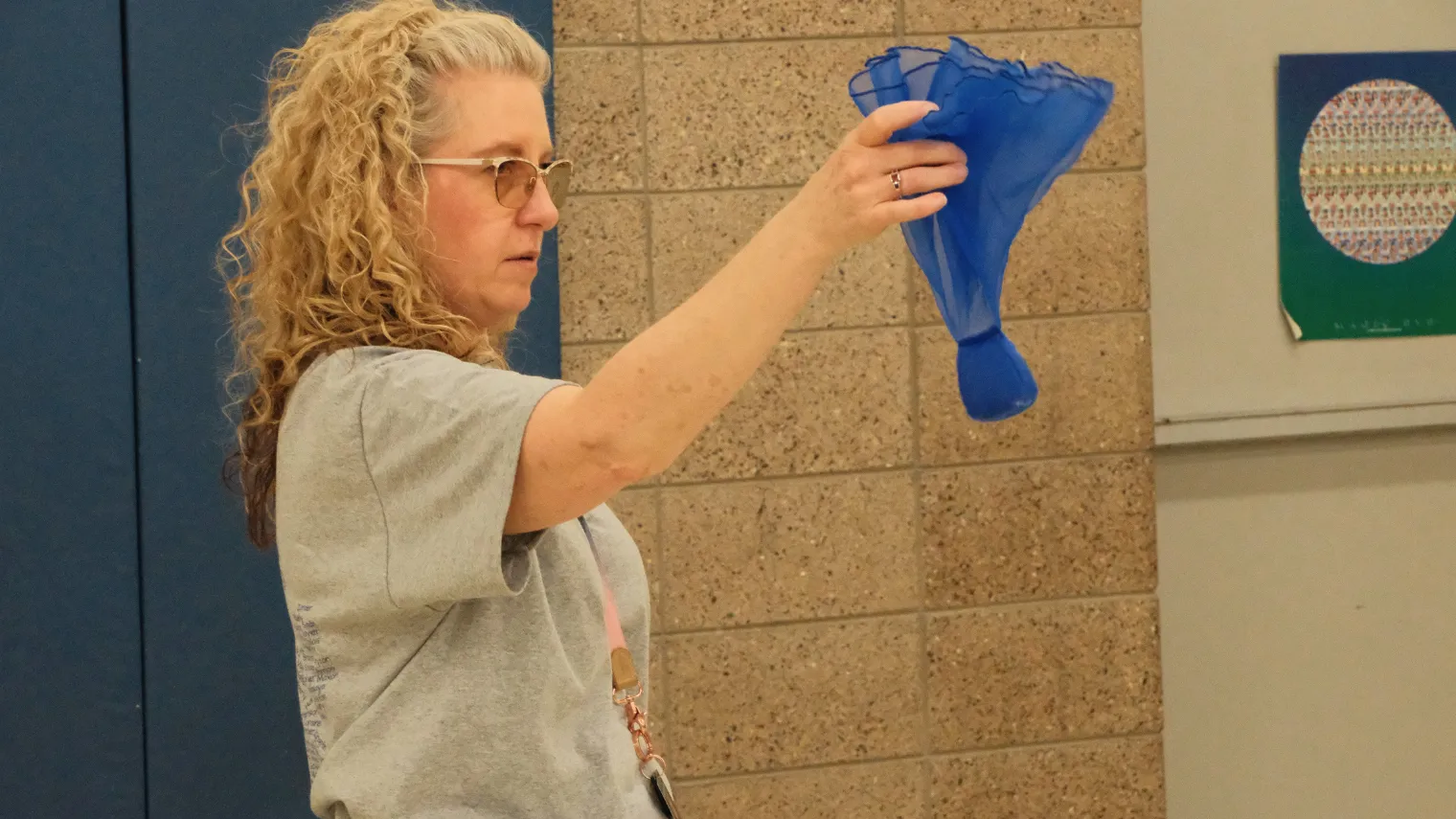 Dawn Ressler holds up a blue beanbag while demonstrating the next activity for elementary students during a physical therapy session.