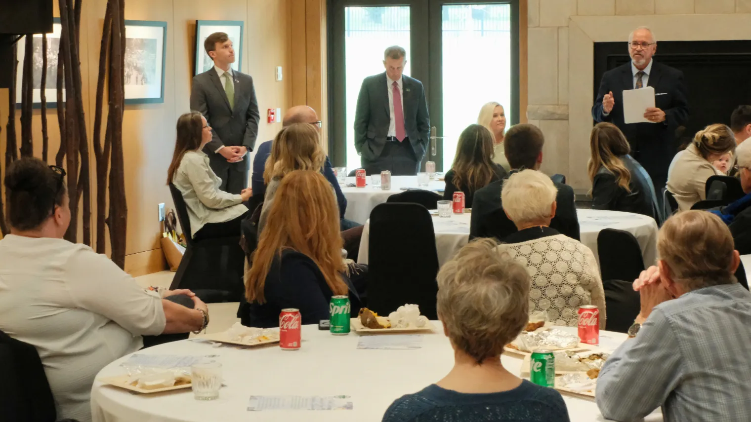 Numerous people sitting around tables, listening to North Dakota United President Nick Archuleta speak at a luncheon in the ND Governor's Residence. 