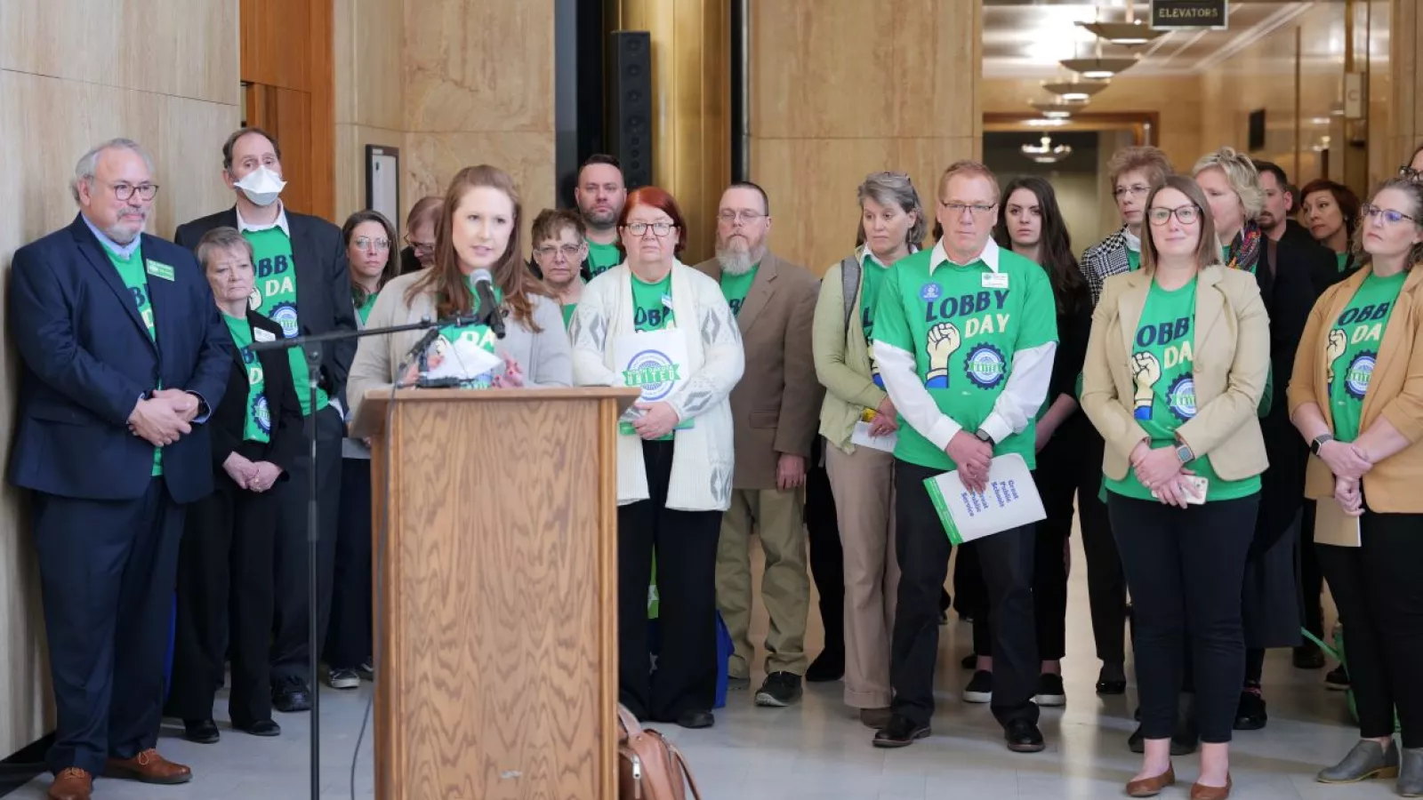 image of a crowd with a woman standing at a podium speaking