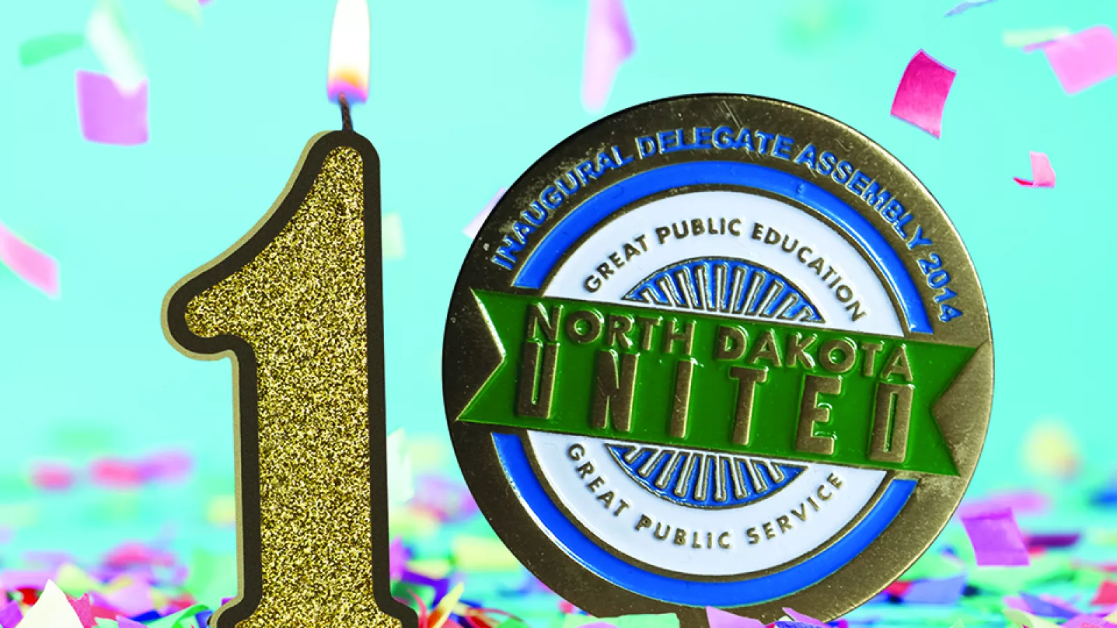 A birthday candle in the shape of the number 1, next to a commemorative coin with the North Dakota United logo, standing together on a light blue background, with brightly colored confetti falling in the background and gathered on the ground.