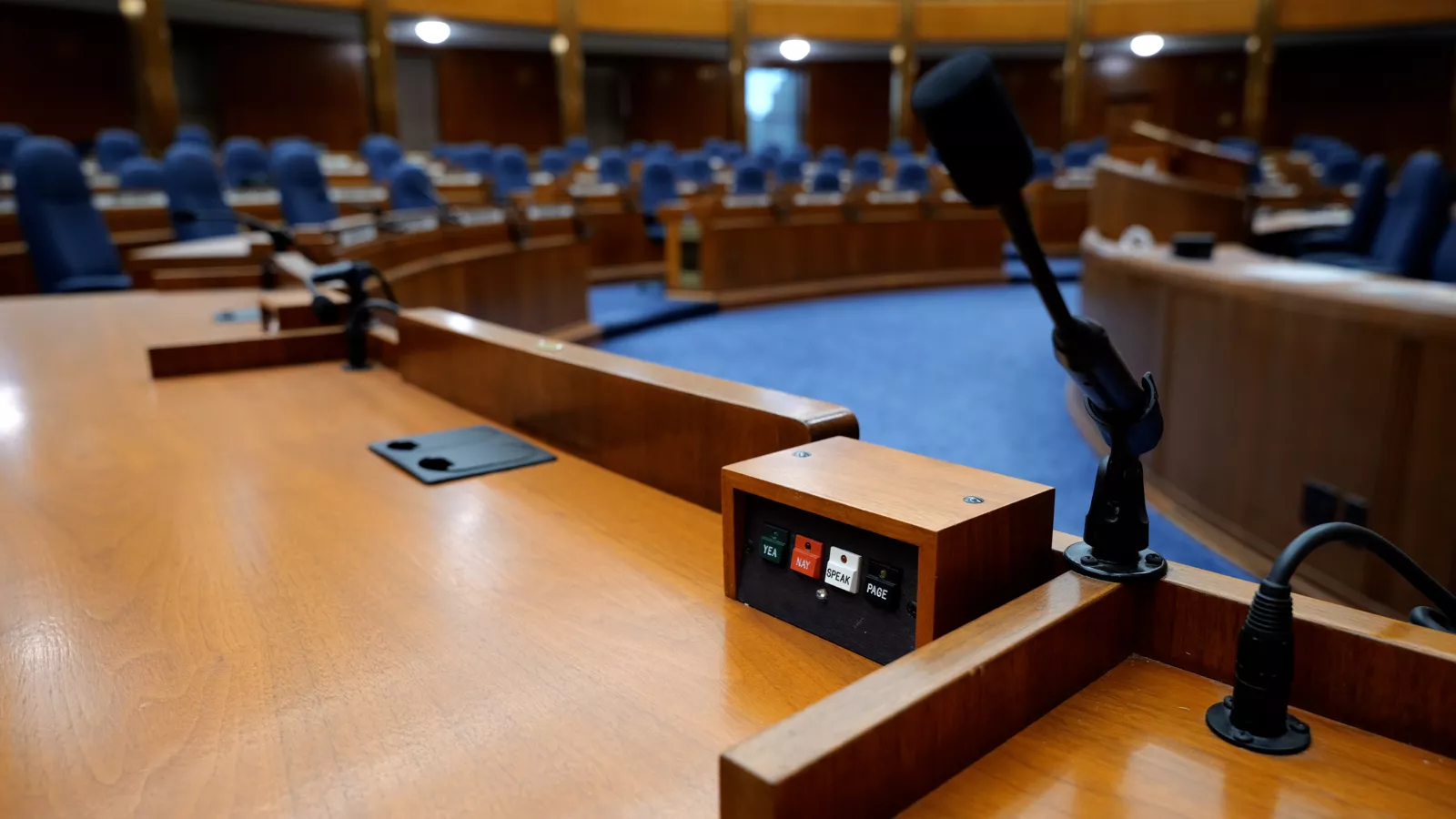 Photo from the perspective of a lawmaker in the North Dakota House of Representatives. The foreground is a microphone and voting panel. The background is the House chamber.
