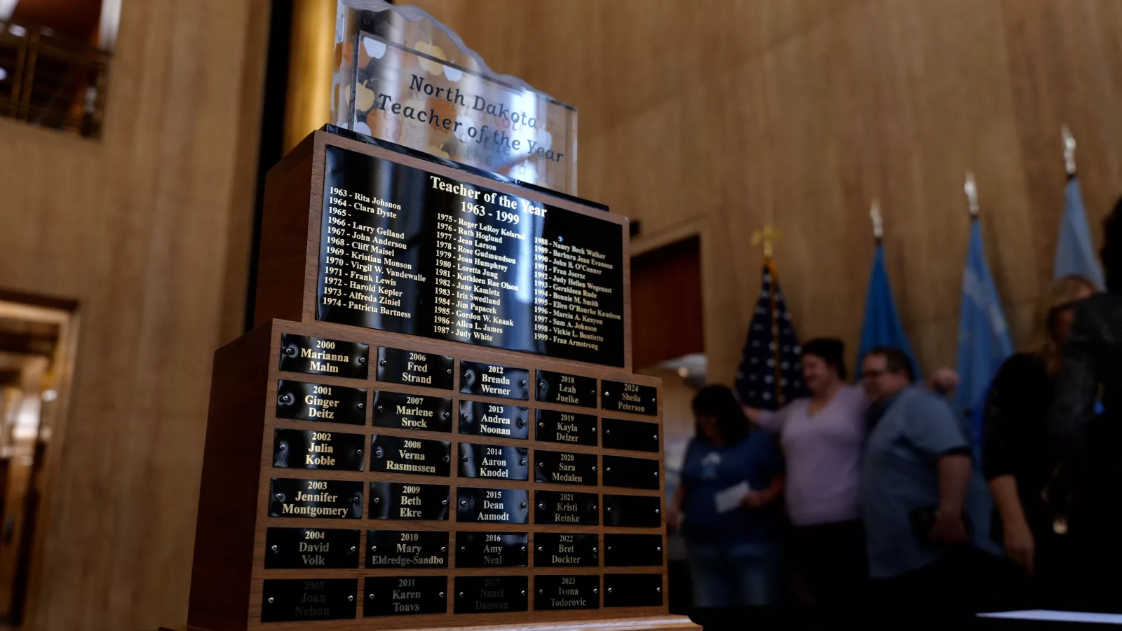 The Teacher of the Year trophy sits in Memorial Hall at the North Dakota State Capitol. The trophy is in the foreground as 2024 Teacher of the Year Sheila Peterson poses in the background with friends