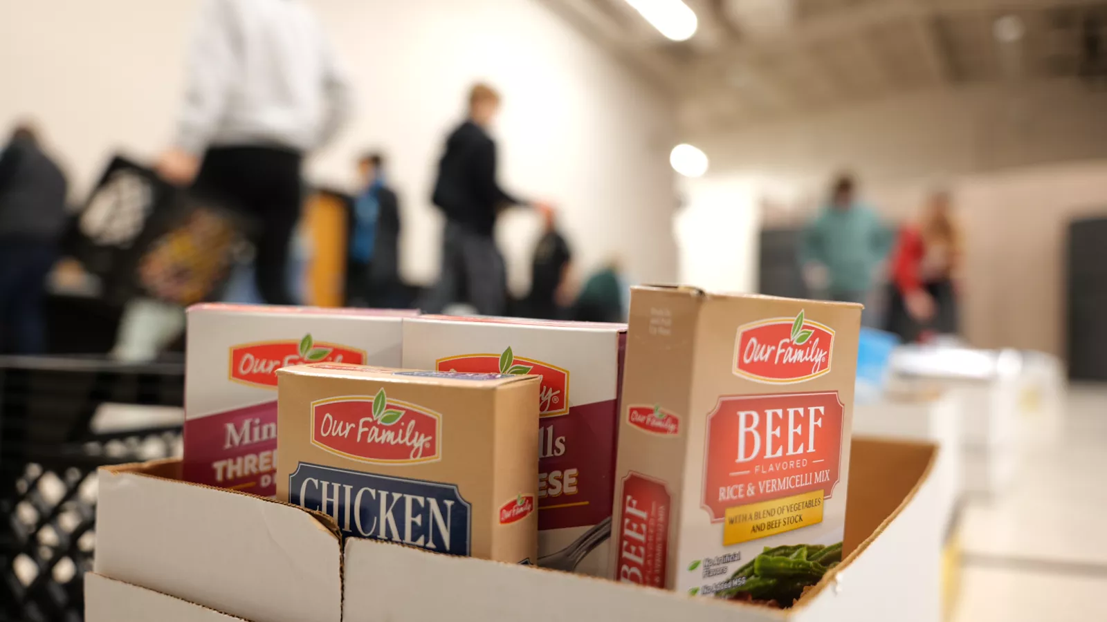Box of of nonperishables in the foreground as many people construct boxes in background