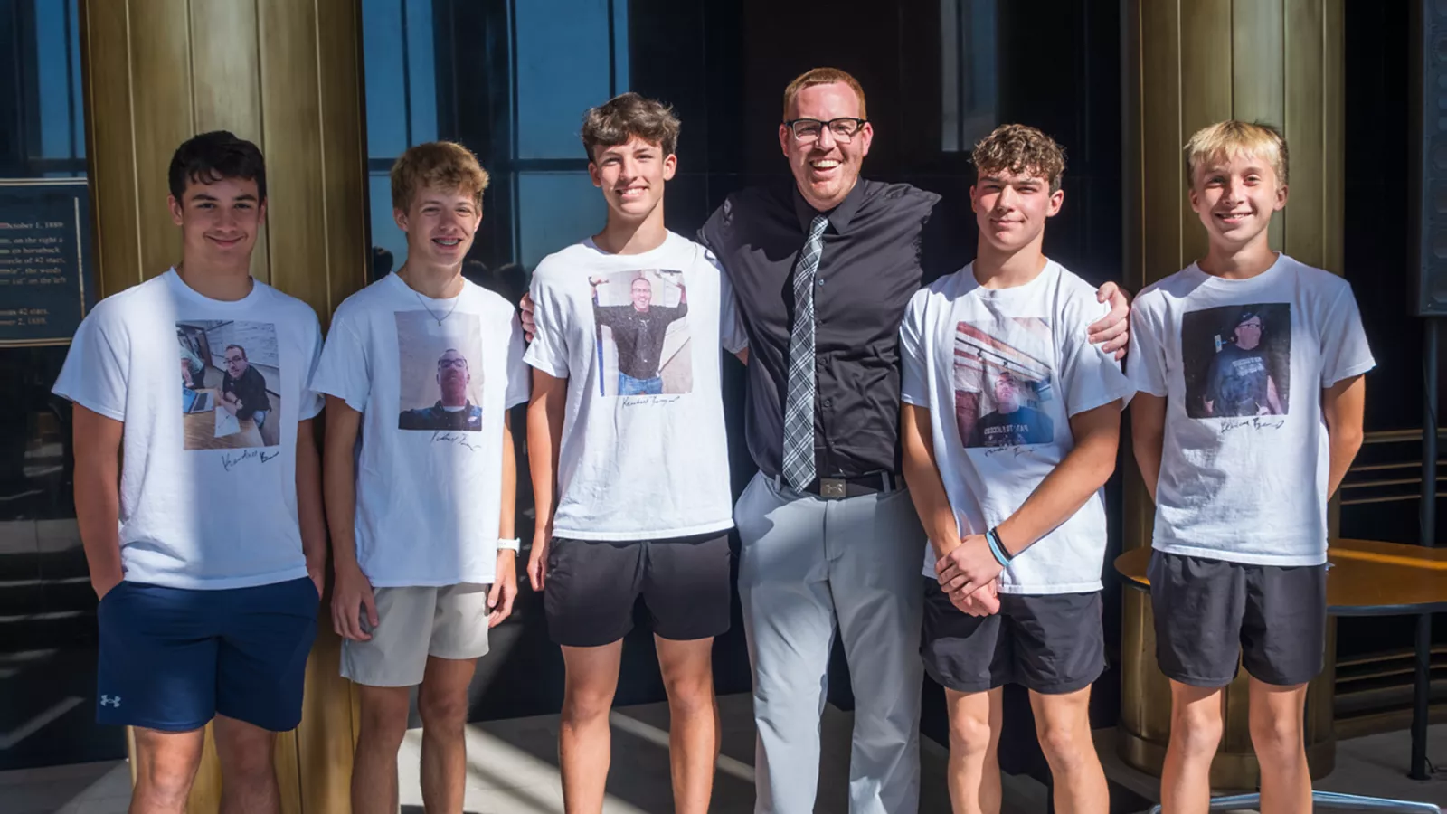 male teacher standing next to students who are wearting t-shirts with his face on them