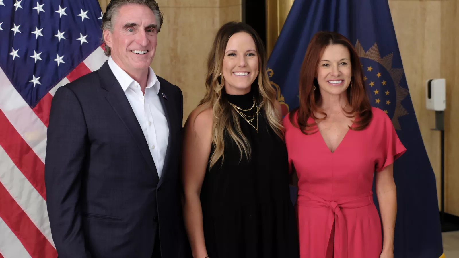 Governor Doug Burgum, Macie Harris-Nelson and Superintendent Kirsten Baesler in front of U.S. and North Dakota flags.