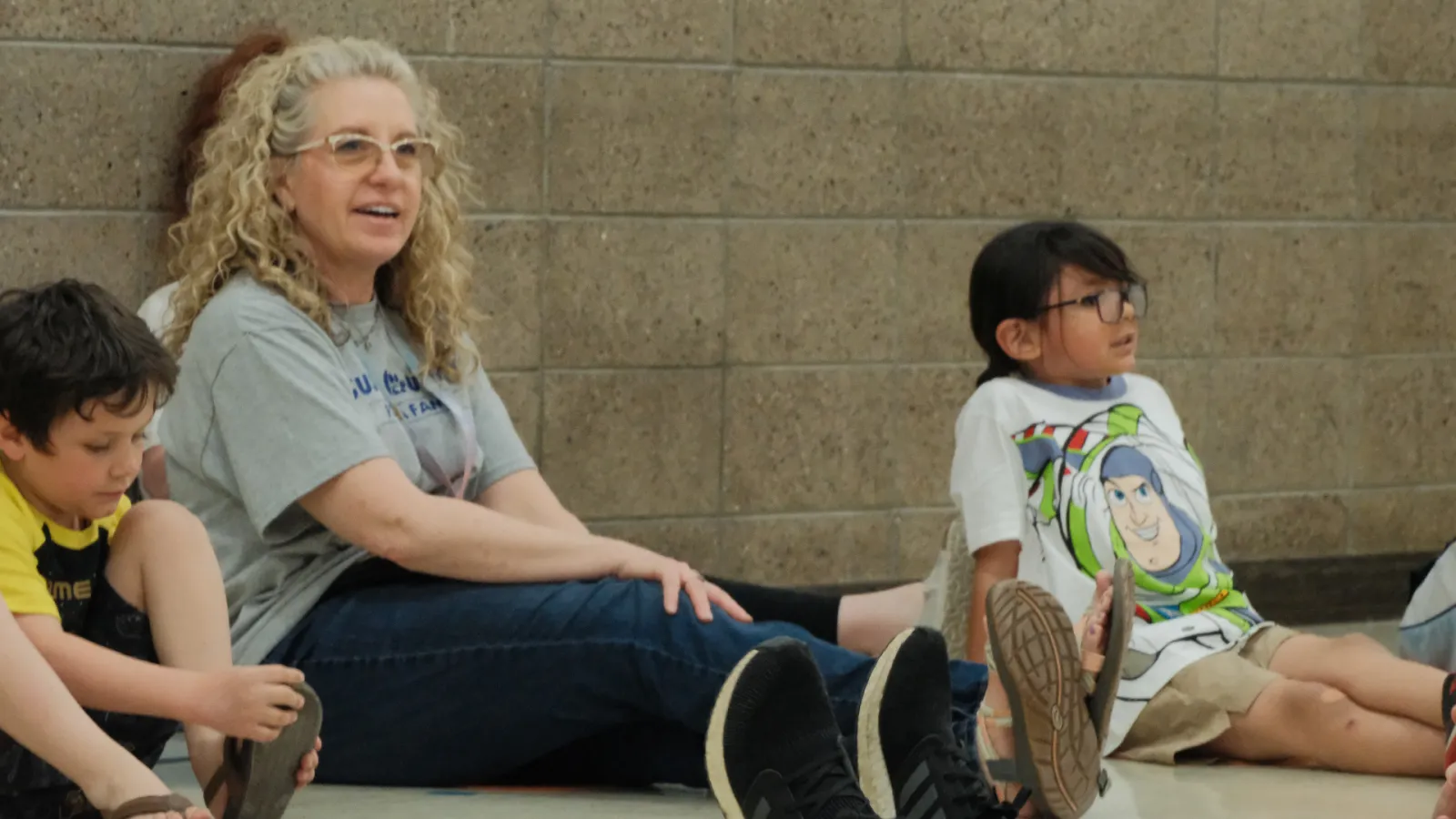 2027 North Dakota United Education Support Professional of the Year Dawn Ressler sits on a gym floor with elementary students during a physical therapy activity at Mandan Public Schools. Ressler smiles as she engages with the children during a playful movement exercise.