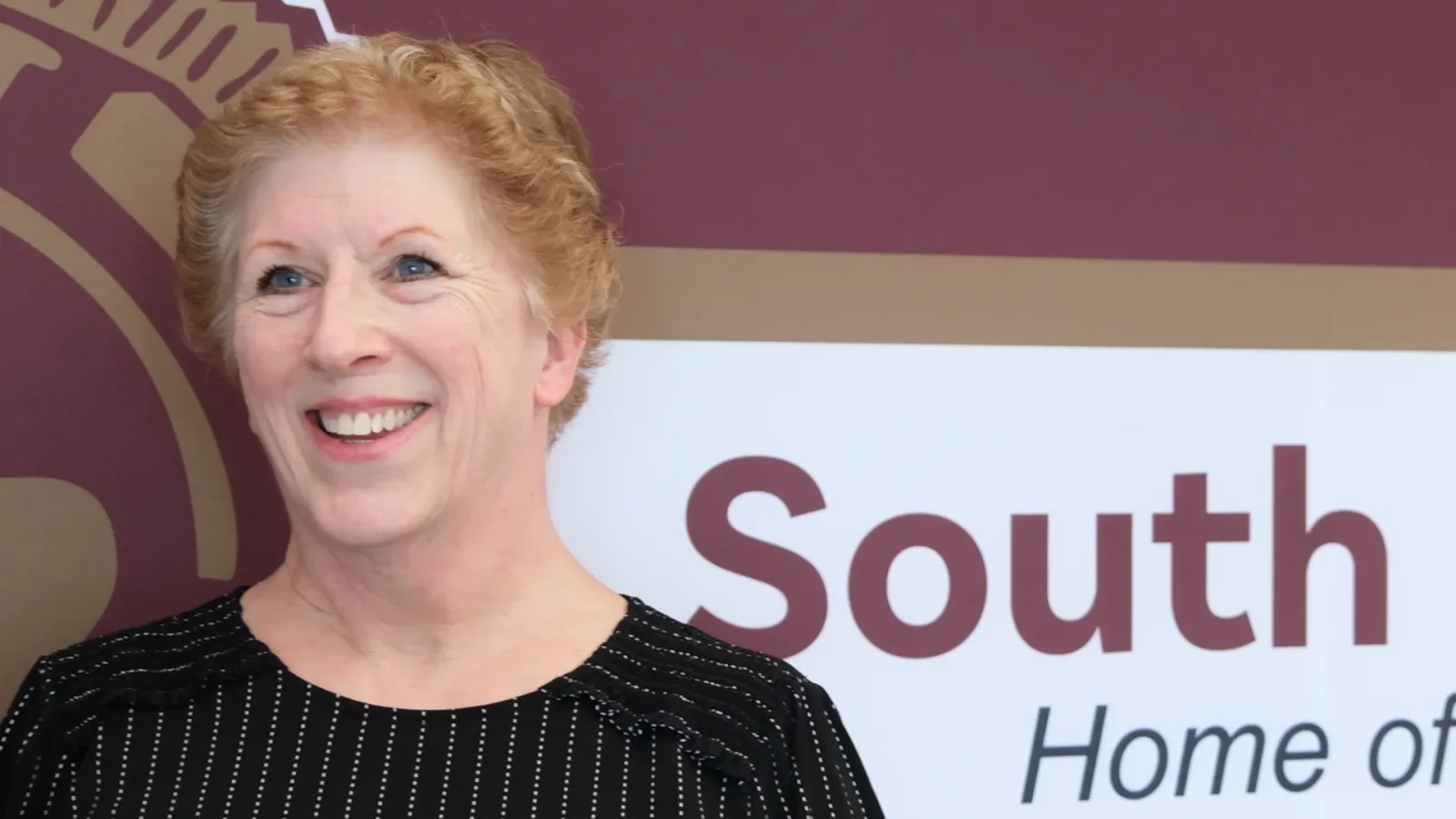 Portrait of Laurie Holcomb, a special education paraprofessional at South Middle School in Grand Forks and a finalist for North Dakota United's 2027 Education Support Professional of the Year. She smiles while standing in front of a school sign.