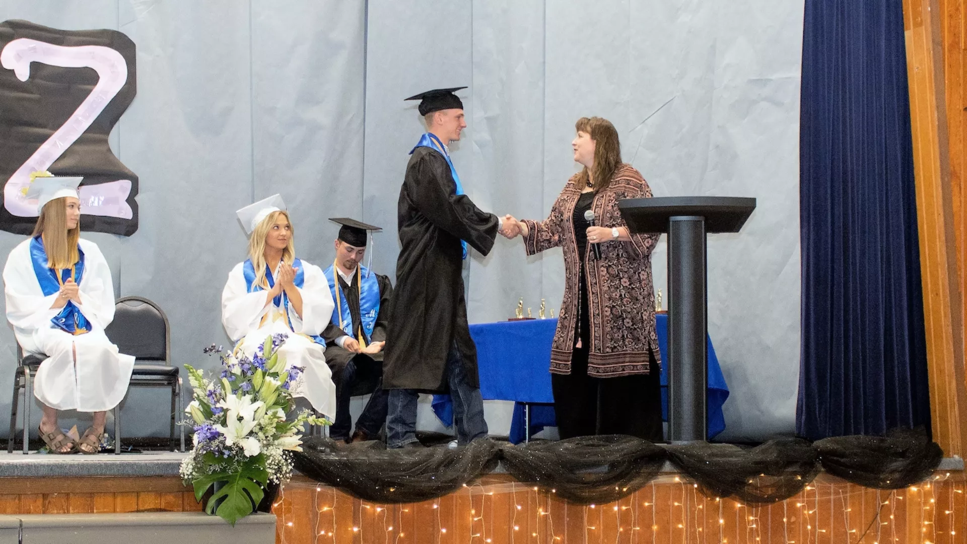 high school student wearing cap and gown getting their diploma