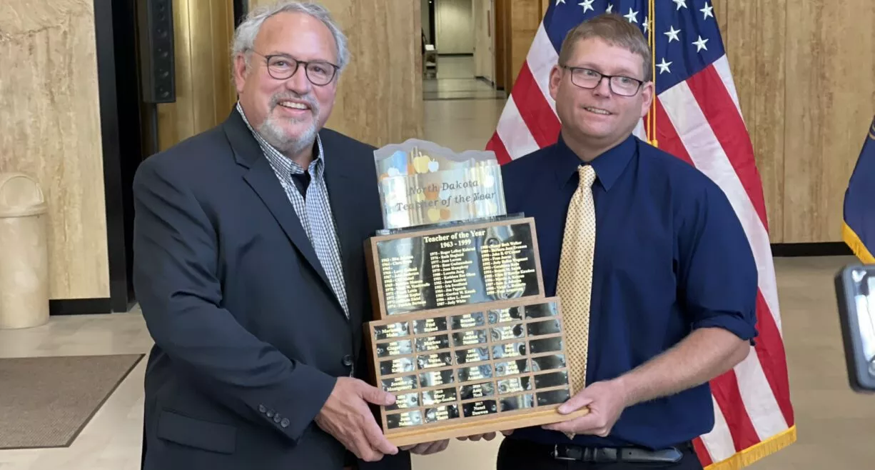 two men in suits holding a large award in front of american flag
