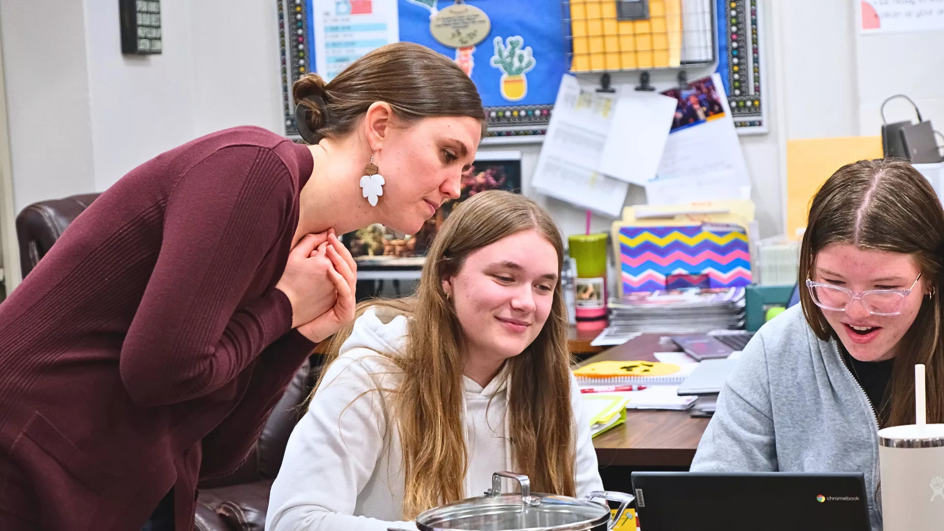 female teacher standing behind students helping them