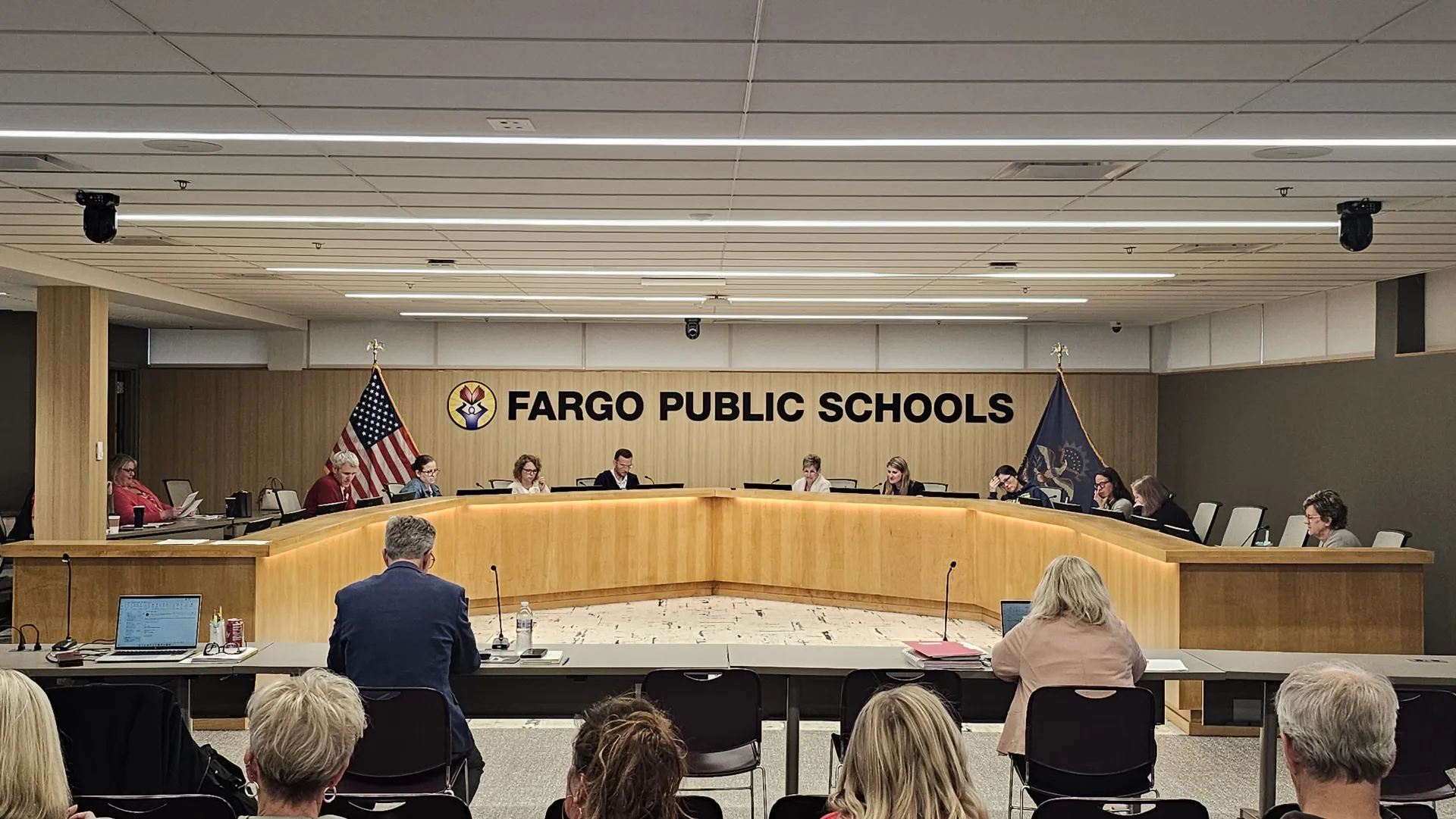 Large group of people gathered in a room with "Fargo Public Schools" written on back wall.
