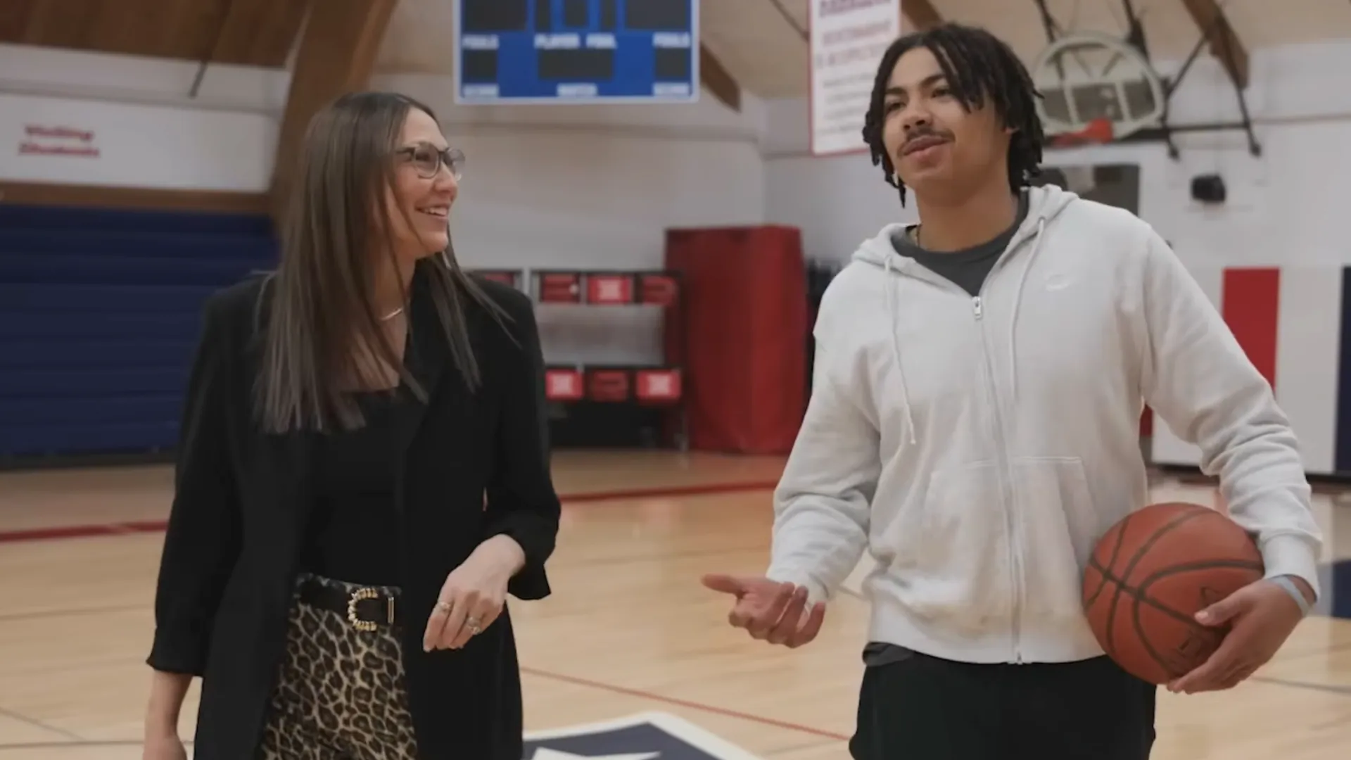 2026 North Dakota Teacher of the Year Frannie Tunseth smiles while walking and talking with May-Port CG Public Schools student Noah Djibonan in the school gym during filming for a North Dakotans for Public Schools advertisement.