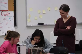 teacher standing looking over students shoulder smiling